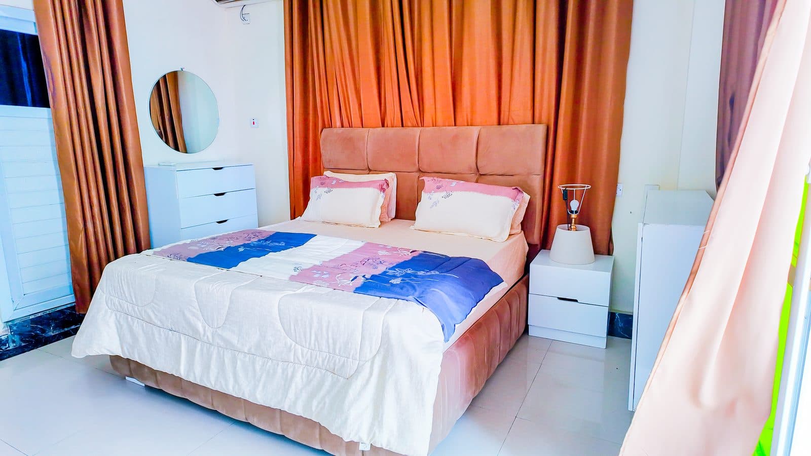 Double bed with a padded headboard, bedside lamp and a white chest of drawers