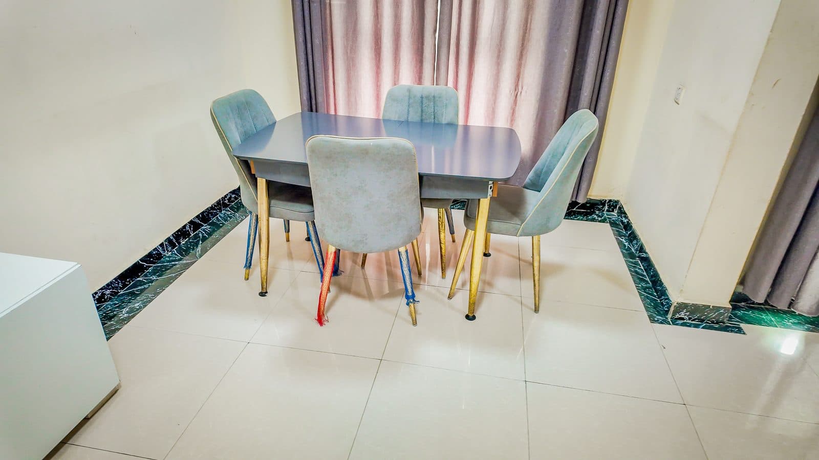 Dining table with four upholstered chairs set against a curtained window