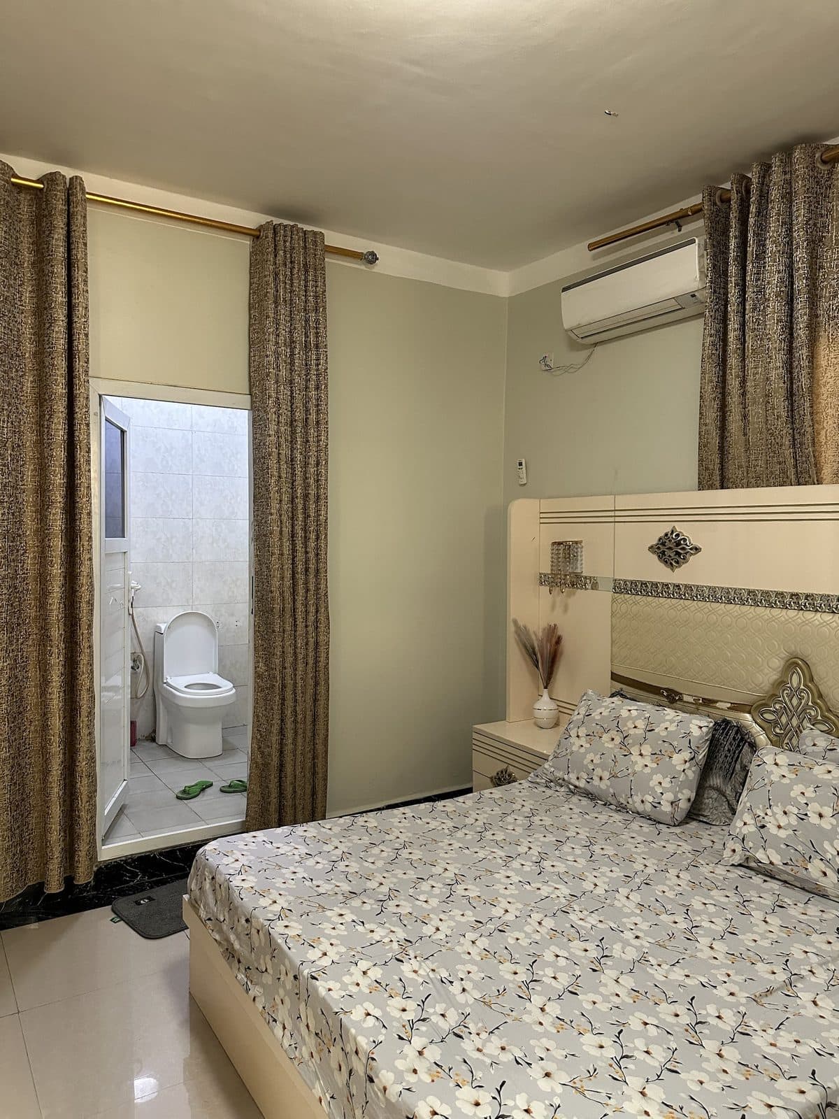 Master bedroom bed with a cream padded headboard, looking through the curtained doorway into the en-suite bathroom