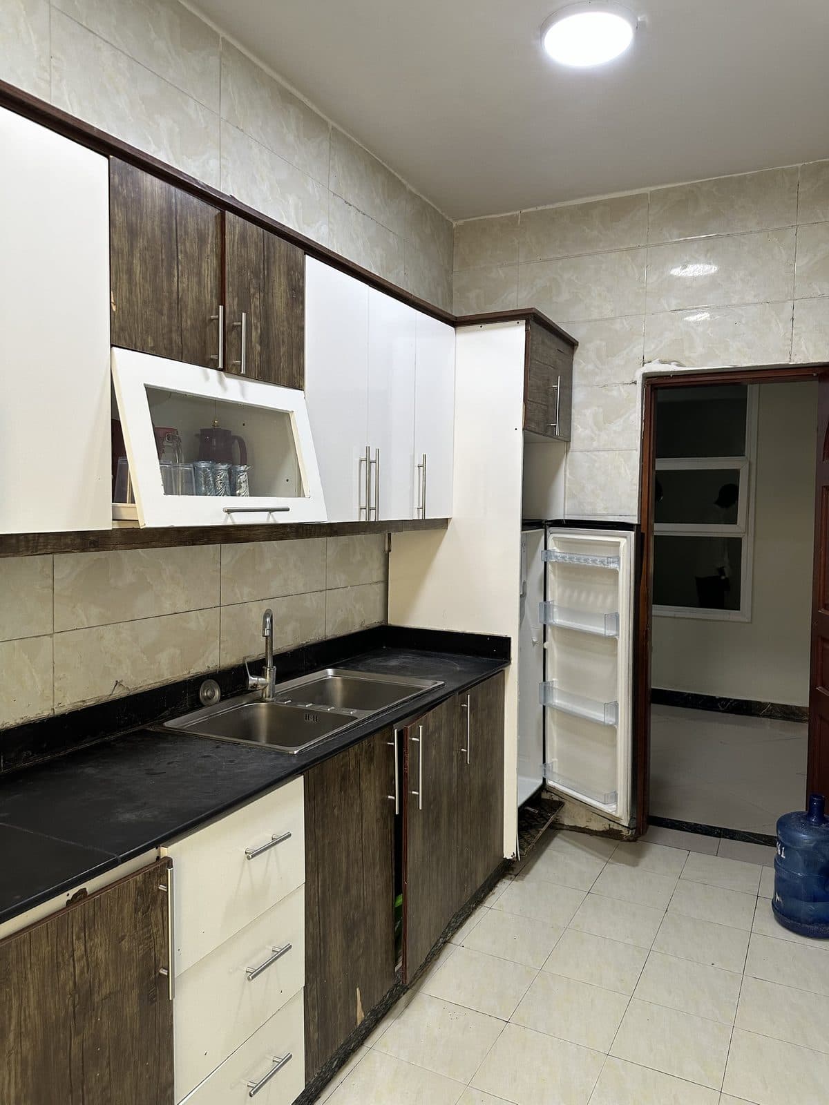 Kitchen with white and dark-wood cabinets, a black worktop with a double stainless-steel sink and a tall fridge