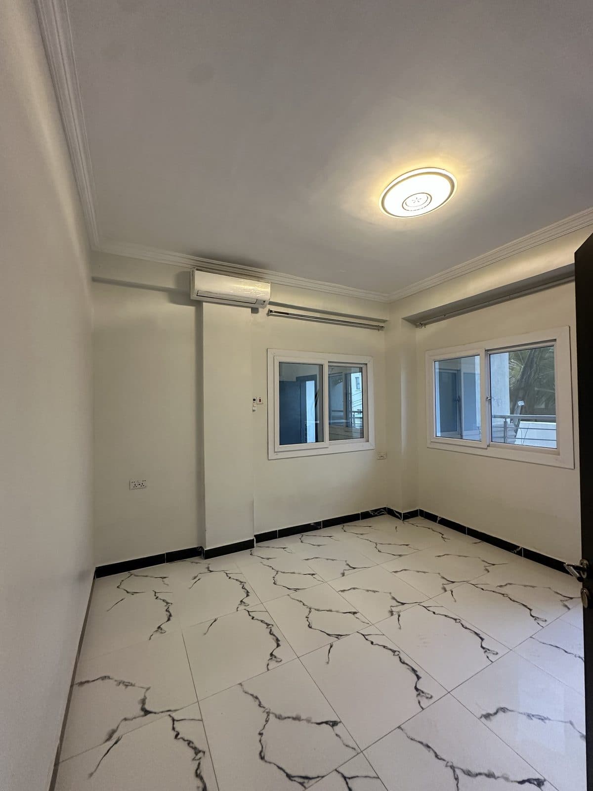 Unfurnished bedroom with a decorative cornice, a round ceiling light, a wall-mounted air conditioner and two windows